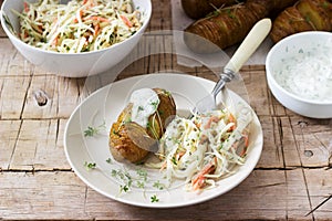 Vegetarian food, hasselback potatoes with sauce and coleslaw on a wooden background. Rustic style.