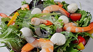 Vegetarian fresh salad with shrimps mozzarella cheese tomatoes arugula peppers rotating on plate. Close up