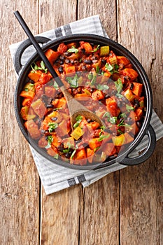 Vegetarian fried sweet potato black bean chili with tomatoes close-up in a pan. Vertical top view