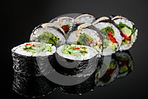 Vegetarian futomaki sushi roll with cucumber, pepper, avocado salad on a black mirror background