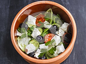 Vegetarian Greek salad with feta cheese, arugula, olives and cherry tomatoes and italian herbs in clay bowl