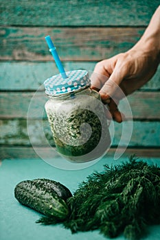 Vegetarian green mix of vegetable and fruit cocktail from cucumber and green parsley and dill. The person takes a jar