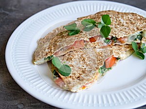 Vegetarian healthy breakfast of melted thin pita bread, cheese, tomato and herbs on a white plate and gray background