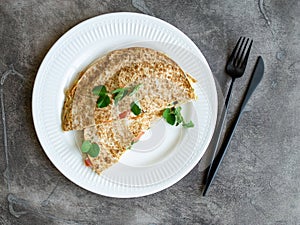 Vegetarian healthy breakfast of melted thin pita bread, cheese, tomato and herbs on a white plate and gray background