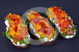 Vegetarian healthy food - eggplants stuffed with cream cheese, green herbs, grilled red and yellow peppers on a black slate backgr
