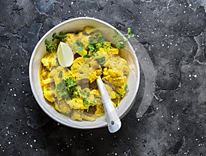 Vegetarian indian cauliflower stew with curry sauce, cilantro, lime on dark background, top view. Delicious indian food concept