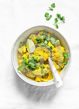 Vegetarian indian cauliflower stew with curry sauce, cilantro, lime on light background, top view. Delicious indian food concept