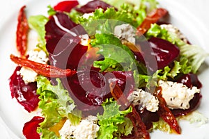 Vegetarian kitchen & healthy food concept. Fresh vegetable salad of sun-fried tomatoes, lettuce, beet and caprine cheese. Close up