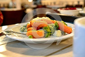 Vegetarian or lenten food. Carrots, cauliflower and green peas on a plate in the kitchen on the table