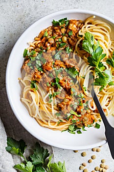 Vegetarian lentils bolognese pasta with parsley in white dish, top view. Healthy vegan food concept