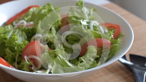 Vegetarian lettuce, onion, tomato and sweet peper salad in a white bowl.