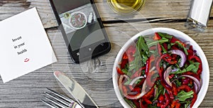 Vegetarian lunch. Salad of fresh vegetables, greens and red sweet peppers with olive oil. On the smartphone screen, a