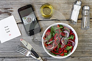 Vegetarian lunch. Salad of fresh vegetables, greens and red sweet peppers with olive oil. On the smartphone screen, a lunch displa