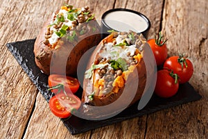 Vegetarian menu baked sweet potato with lentils served with sour cream and tomatoes close-up on a slate board. horizontal