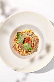 Vegetarian pasta with basil and tomatoes on white plate. Tomato pasta in summer menu with hard shadows Spaghetti with tomatoes on