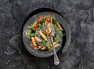 Vegetarian penne pasta with green beans and tomato sauce on a dark background, top view