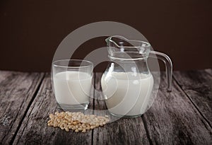 Vegetarian pine nut milk in a glass cup and jug on wooden background. Horizontally