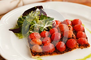 Vegetarian pizza with cherry tomatoes, served with fresh herbs on a round white plate. on a wooden table top decorated with