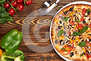 Vegetarian pizza with vegetables at brown wooden table top with ingredients and cutlery with copy space