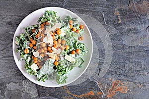 Vegetarian plant based Caesar salad with chickpeas, kale and a yogurt dressing. Top down view on a slate background.