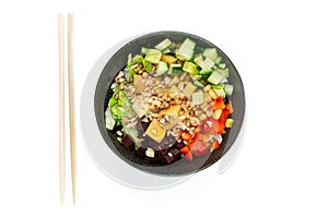 Vegetarian poke bowl in design black bowl with chopsticks below, isolated on white background. Green cucumber, red pepper, peanuts