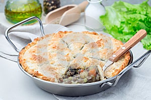 Vegetarian pot pie with lentil, mushroom, potato, carrot and green peas, covered with puff pastry, in baking dish, horizontal