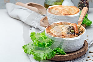 Vegetarian pot pie with lentil, mushroom, potato, carrot and green peas, covered with puff pastry, in baking dish, horizontal,