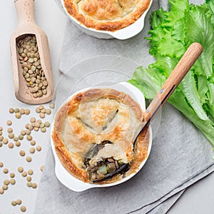 Vegetarian pot pie with lentil, mushrooms, potato, carrot and green peas, covered with puff pastry, in baking dish, square, top