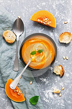 Vegetarian pumpkin cream soup on a gray background. The soup is served with toasted bread. The concept of autumn. The view from ab