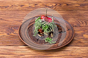 Vegetarian salad with eggplant and arugula in a plate on a wooden background