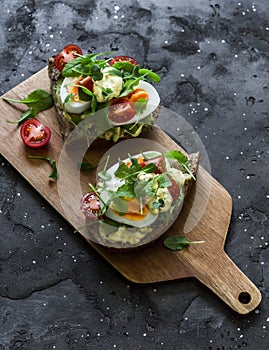 Vegetarian sandwiches with grain bread, avocado, boiled egg, micro-greens, cherry tomatoes and homemade mayonnaise on a cutting