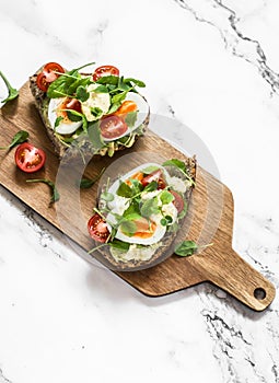 Vegetarian sandwiches with grain bread, avocado, boiled egg, microgreens, cherry tomatoes and homemade mayonnaise on a cutting