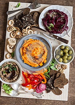 Vegetarian snack table. Pumpkin, beets hummus, beans and mushroom pate, vegetables, nuts, bread on a wooden table, top view.