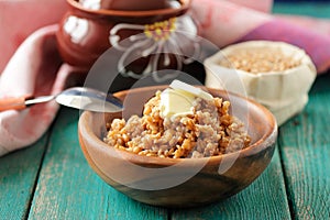 Vegetarian spelt porridge with butter in wooden bowl and raw spelt in linen bag on turquoise table