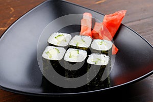 Set sushi rolls with ginger on a black plate on a dark wooden background.