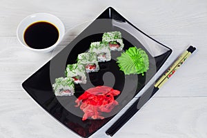 Vegetarian sushi rolls on a black square plate with wasabi, soy sauce and ginger. White wooden background