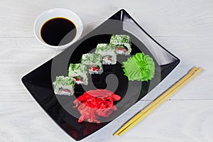 Vegetarian sushi rolls on a black square plate with wasabi, soy sauce and ginger. White wooden background