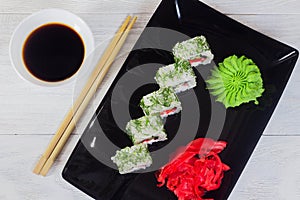 Vegetarian sushi rolls on a black square plate with wasabi, soy sauce and ginger. White wooden background