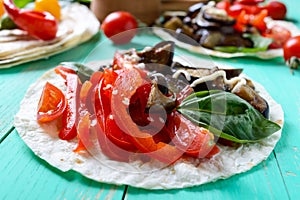 Vegetarian tacos with eggplant, cherry tomatoes, sweet peppers on a bright wooden background.