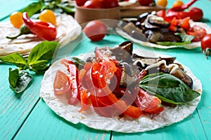 Vegetarian tacos with eggplant, cherry tomatoes, sweet peppers on a bright wooden background.