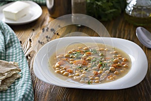 Vegetarian thick cheakpea soup with corrots and greens in white plate on wooden table with ingredients around. Turkish and greek photo