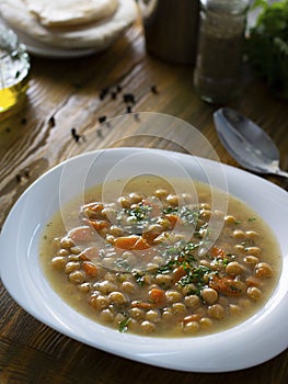 Vegetarian thick cheakpea soup with corrots and greens in white plate on wooden table with ingredients around. Turkish and greek photo