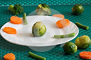 Vegetarian vegetables: broccoli, Brussels sprouts, carrots and green beans on a white plate and green background