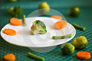 Vegetarian vegetables: broccoli, Brussels sprouts, carrots and green beans on a white plate and green background