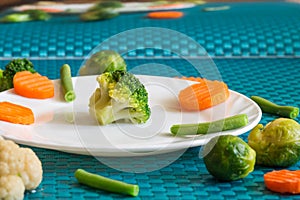 Vegetarian vegetables: broccoli, Brussels sprouts, cauliflower, carrots and green beans on a white plate and blue