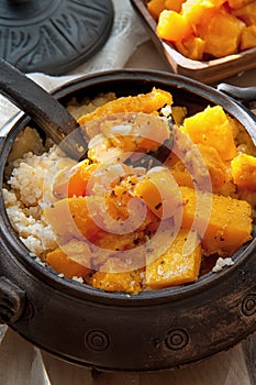 Vegetarian wheat porridge with large bright orange pieces of juicy fried pumpkin in a clay pot in a rustic style organic food