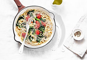 Vegetarian whole grain spaghetti pasta with cherry tomatoes and spinach sauce in a cast iron pan on a white background, top view.