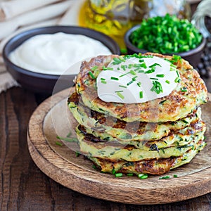 Vegetarian zucchini fritters or pancakes, served with greek yogurt and green onion on wooden plate, square format