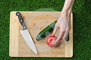 Vegetarians and cooking on the nature of the theme: human hand holding cucumber, tomato on a cutting board and a background of gre