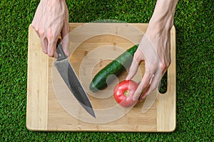 Vegetarians and cooking on the nature of the theme: human hand holding cucumber, tomato on a cutting board and a background of gre